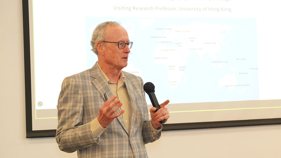 Older man in plaid blazer speaks with a microphone before a slide reading Visiting Research Professor, University of Hong Kong.