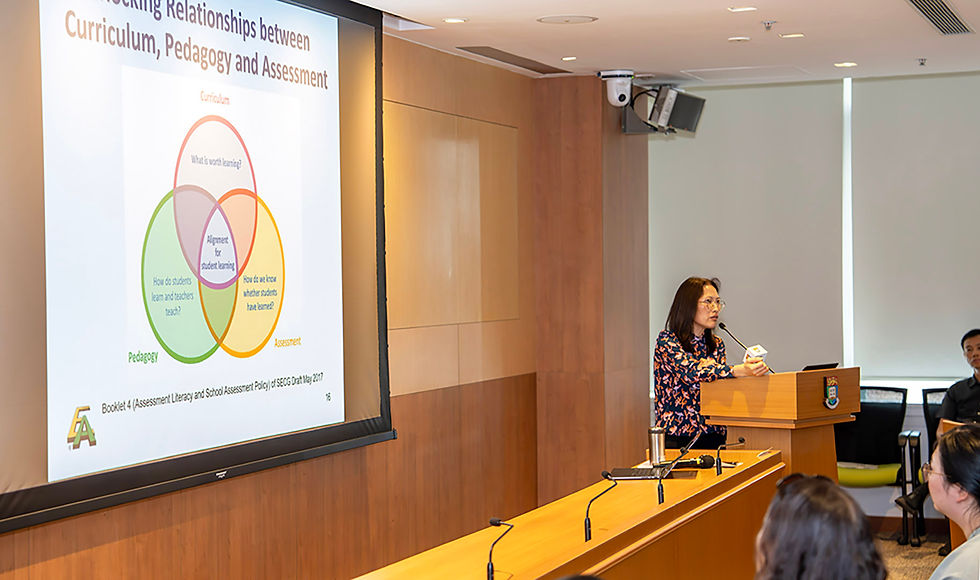 Woman presents at podium in lecture room beside slide titled Curriculum, Pedagogy and Assessment with Venn diagram
