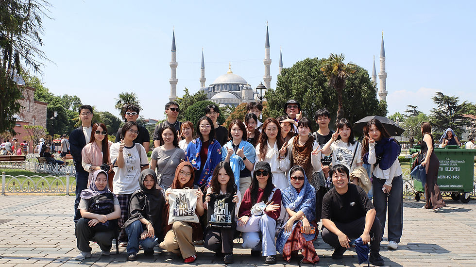 Group of smiling tourists posing in front of the Blue Mosque in Istanbul, with minarets and trees under a clear sky.