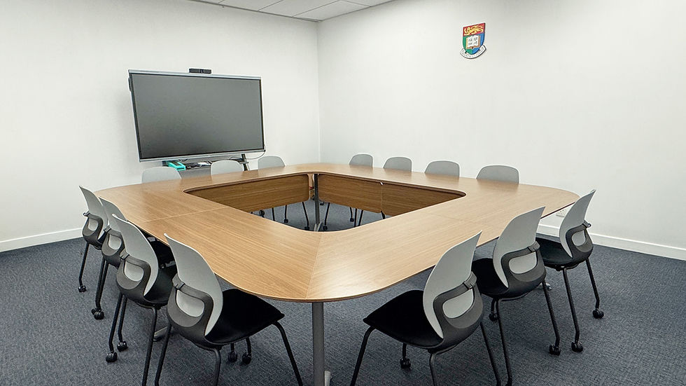 Empty modern conference room with U-shaped wood table, gray chairs, large screen, and a crest on the wall.