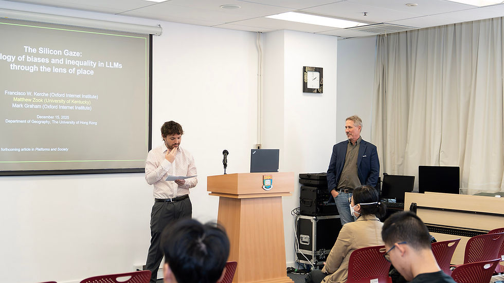 Lecture room with two presenters by a podium and projected slide titled The Silicon Gaze, audience seated in red chairs.