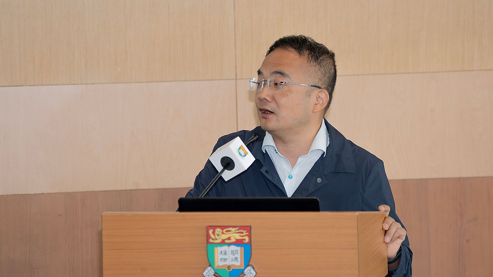 Man in glasses speaks at a podium with a microphone, in front of a wood-paneled wall and crest, looking focused.