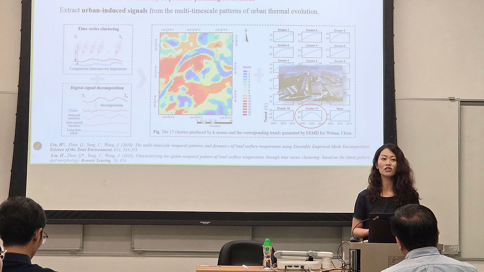 Presenter speaks in a classroom beside a projected slide of urban thermal evolution maps, charts, and Wuhan data.