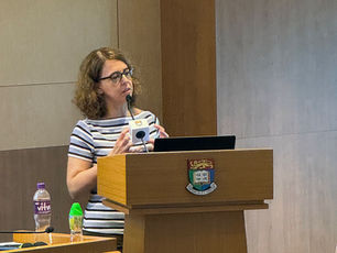 Woman in striped shirt speaks at a lectern with a microphone and laptop in a lecture room, looking focused.
