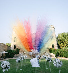 Mariés célébrant devant un château avec jets de poudre colorée, mariage festif dans l’Hérault Occitanie.