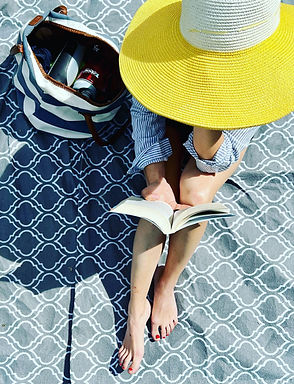 Kvinne med hatt leser bok på stranden