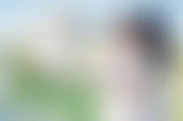 Din embraces Rose from behind on their wedding day at their farm, the couple standing together in soft sunlight with a gazebo in the background.