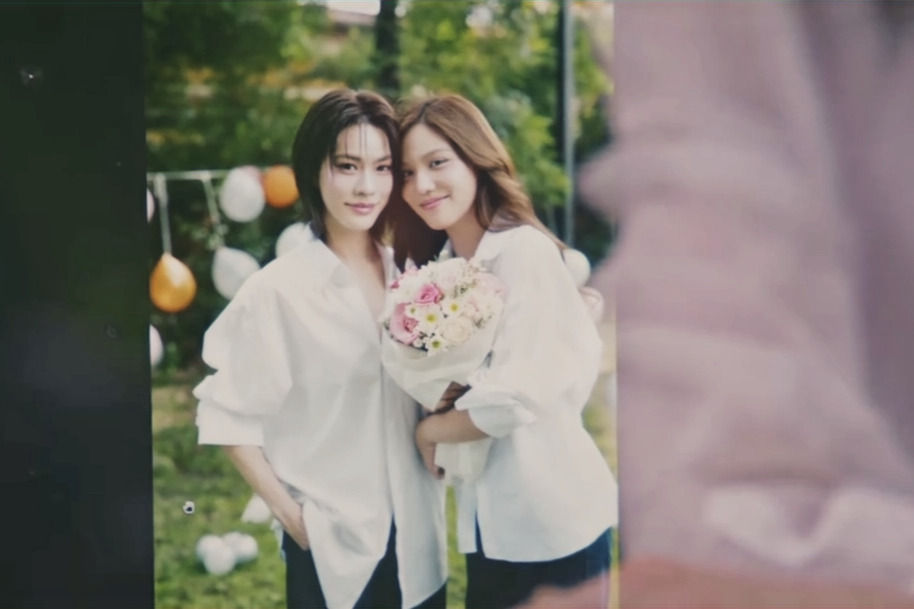 Chan and Key pose closely together in white shirts, smiling and holding a bouquet during their outdoor photoshoot with Peach.