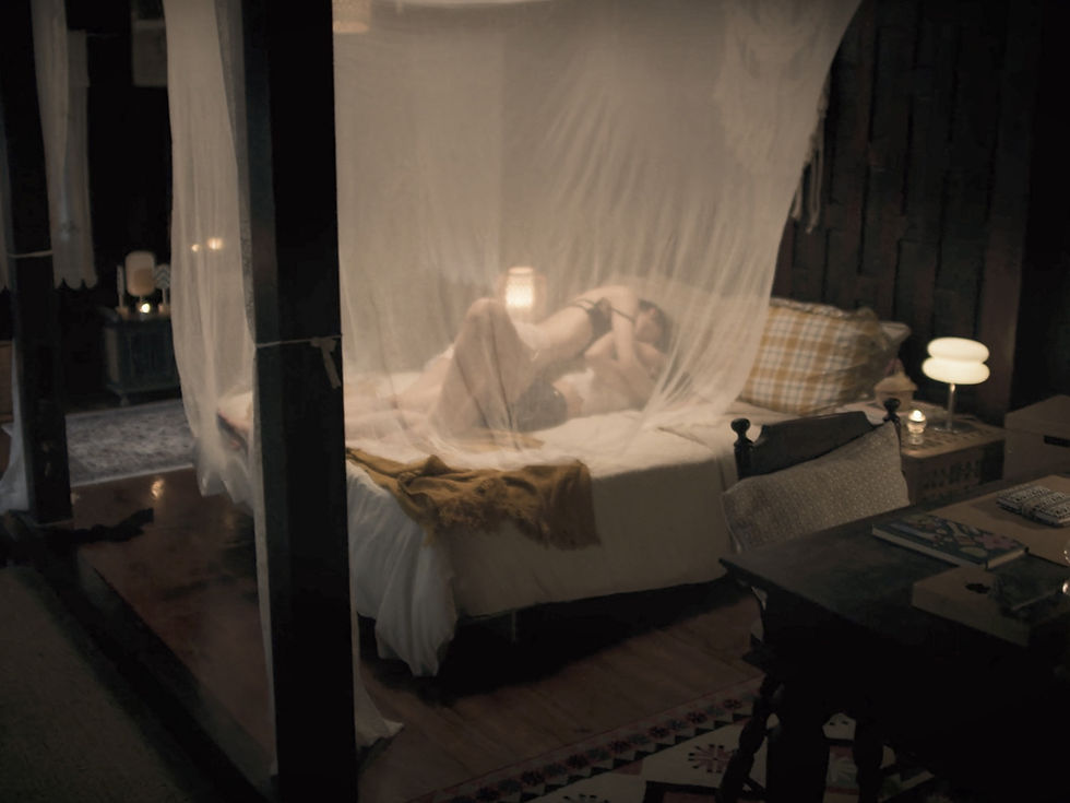 Klao and Si share a tender, intimate moment on a bed beneath a sheer canopy, surrounded by soft lighting and a cozy room setting.