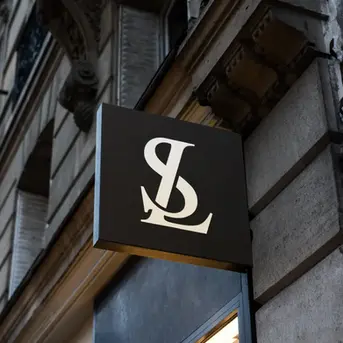 Monogram signage design with overlapping letters 'S' and 'L' displayed on a black storefront sign in a classic European setting.