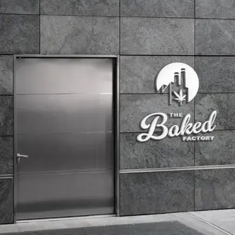 Modern industrial logo design for The Baked Factory displayed on a stone building facade, featuring smokestacks and a cannabis leaf.
