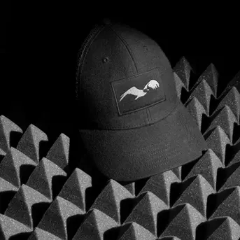 Embroidered logo on black baseball cap with a minimalist bird design, displayed on acoustic foam background for a premium brand look.