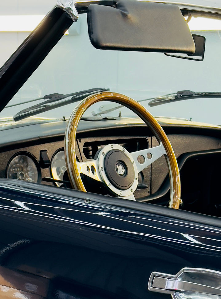 RS.IKON präsentiert: Triumph Spitfire Mk4 – Detailaufnahme des Innenraums von der Seite, stilvolles Holzlenkrad im Mittelpunkt, perfekter Klassiker.