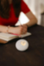 Person schreibt ins Dankbarkeitstagebuch, davor Achtsamkeitslicht mit Herzsymbol