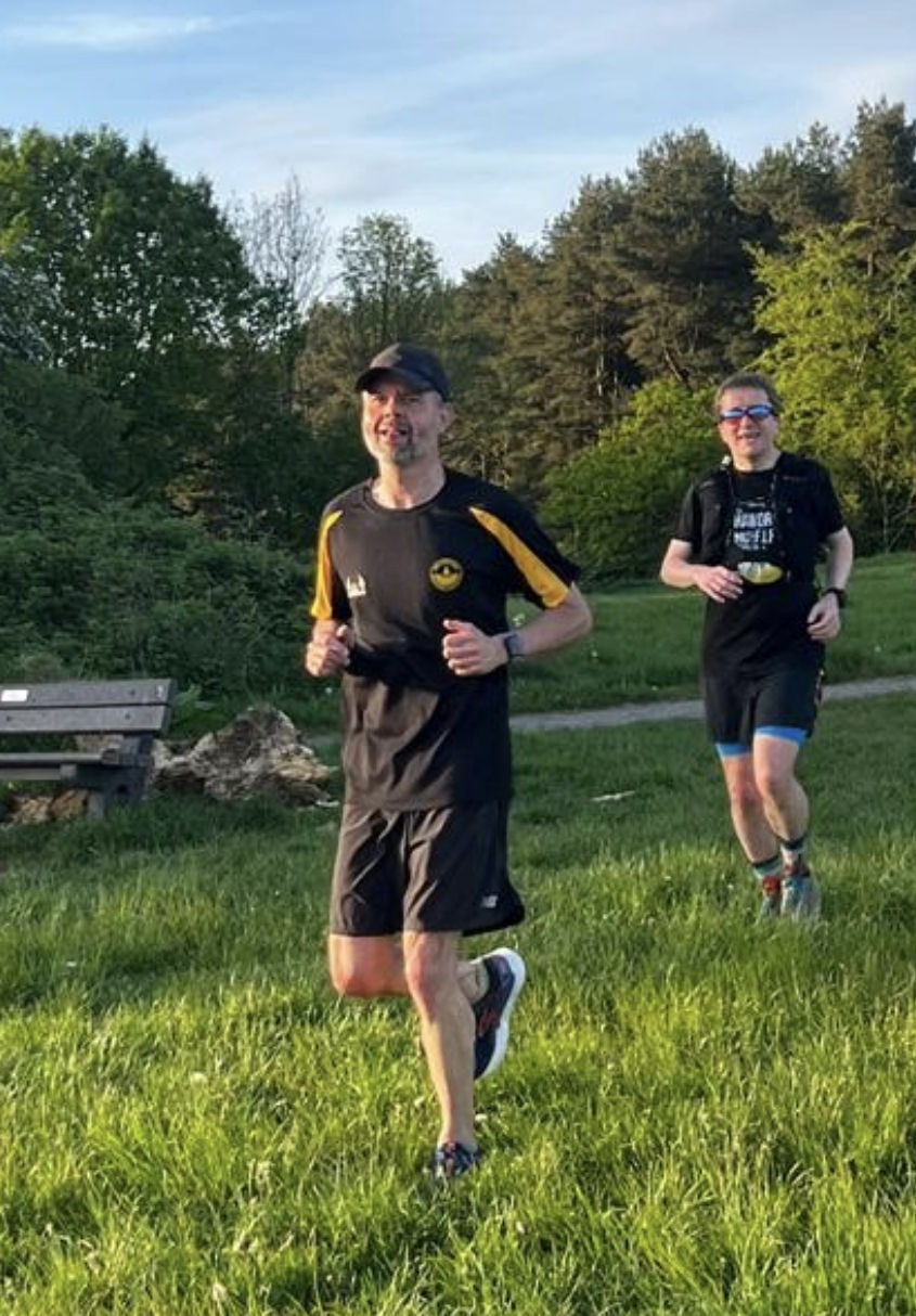 male runner in black and yellow tee and black cap running on grass