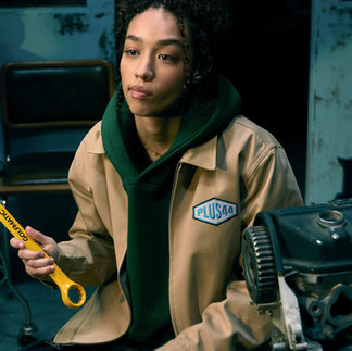 A girl poses with a wrench modeling a jacket from Lewis Hamilton's +44 collaboration with Tyler, The Creator's Golf Wang.
