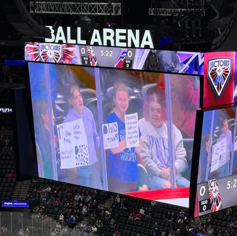 A girl holds up a sign that says "Hensley, I share your faith and you really inspire me. Selfie" on the Ball Arena video board.