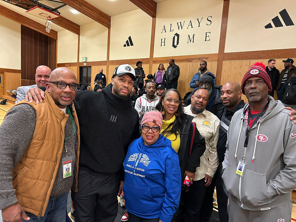 Damian Lillard poses with members of the Oakland community at Ira Jinkins Recreation Center in front of a sign that says "Always Home"
