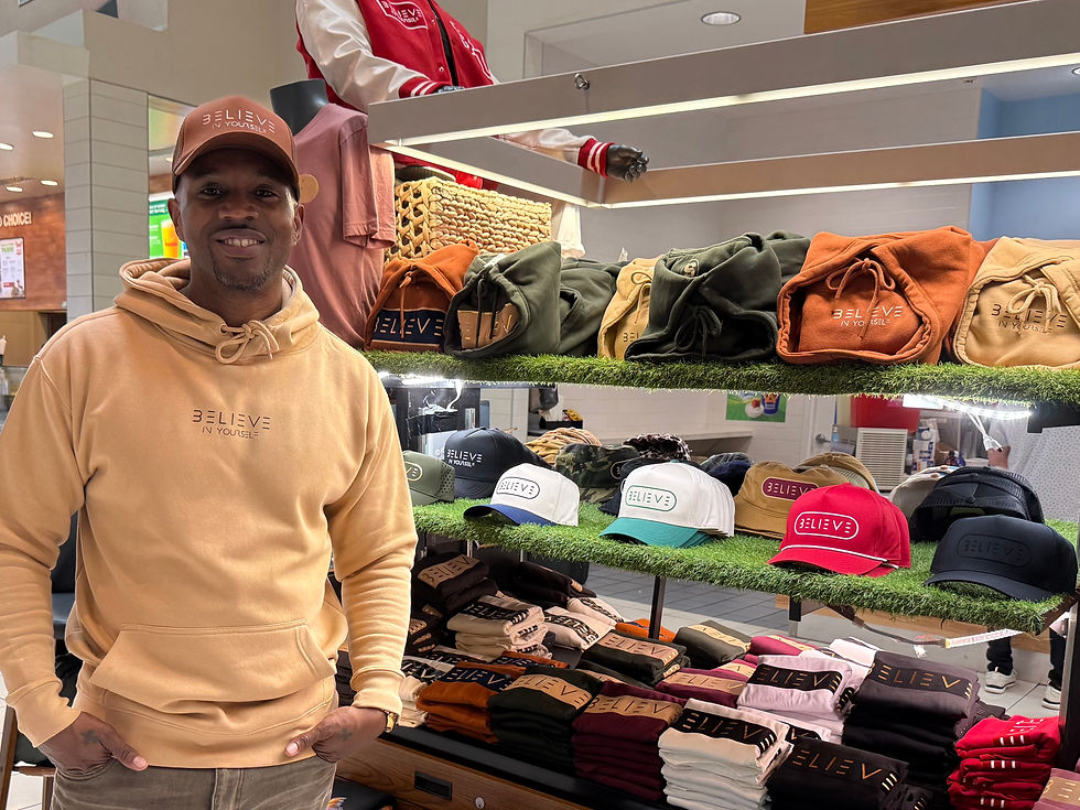 A man poses in front of a mall kiosk of hats and T-shirts.