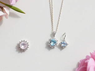 Soft, minimalist flat lay of fine jewelry featuring delicate rings, necklaces, and earrings with pastel gemstones in powder pink, lavender, and sky blue, arranged on a simple light gray background with soft natural lighting, highlighting a refined True Summer color palette aesthetic.