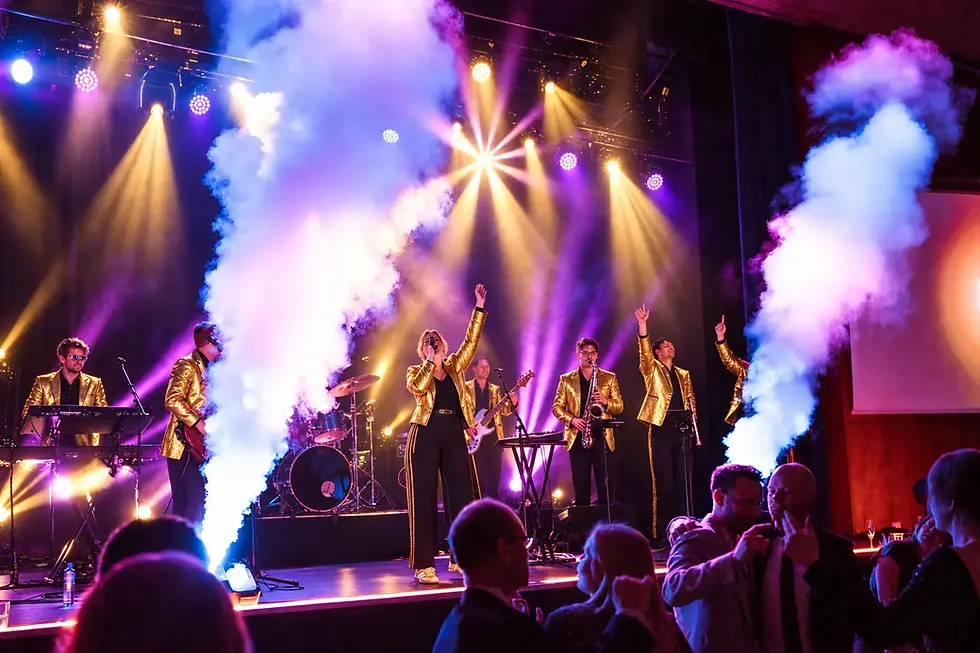Partyband i gulljakker spiller foran publikum med scenelys og røykeffekter
