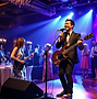duo med mannlig vokalist og gitarist og kvinnelig vokalist som synger blant gjestene under ulebord og firmafest i Trondheim med glade og engasjerte gjester i bakgrunnen
