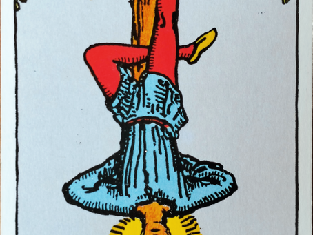 The Hanged Man of the Rider-Waite Tarot, which is a man in red tights and a blue tunic suspended upside down on branches forming a T-shape.