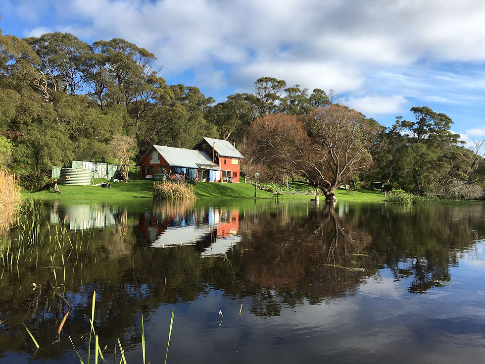 Two-storey cedar wood house by a lake with trees behind.