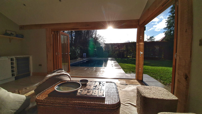 Corner bifold doors open leading out to a garden swimming pool