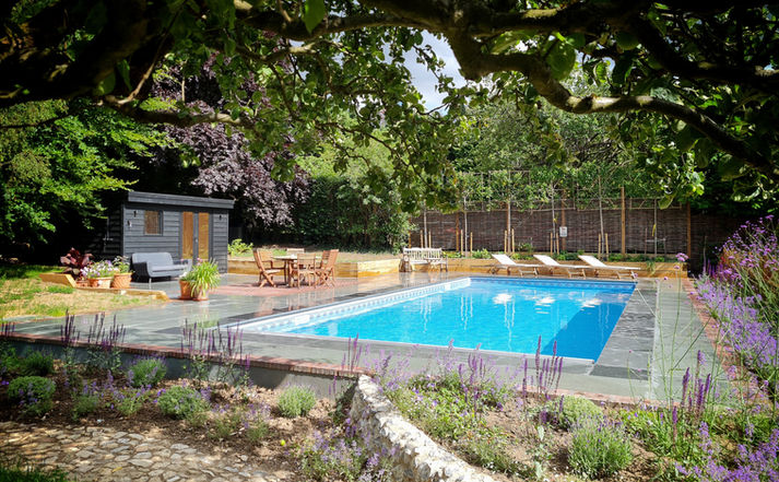 garden pool area surrounded by mediterranean plants, espalier trees and dark grey wooden pool outbuilding