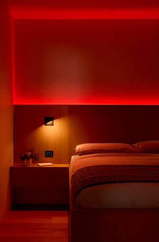 Red bedroom lighting softly glowing from a custom wooden headboard
