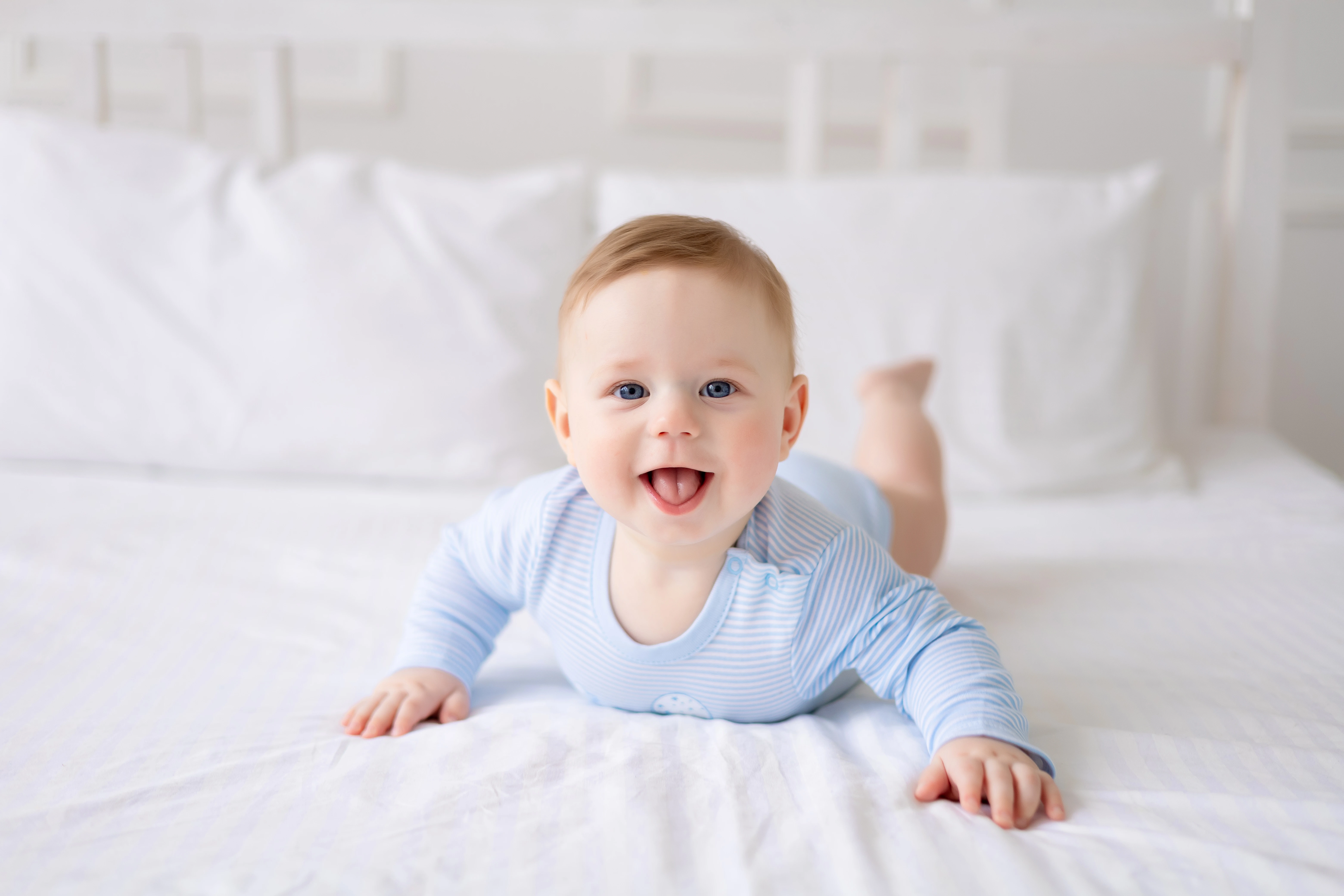 un-bambino-carino-e-sano-e-sdraiato-su-un-letto-su-lenzuola-bianche-a-casa-in-un-body-blu-