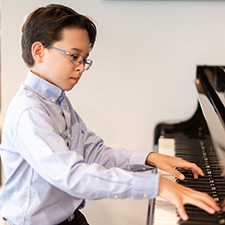 Young composer Bradley Carpiuc, Age 10, plays the piano wearing a long sleeve white collar shirt.