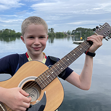 Headshot of Lundy Frishman holding his guitar in front of a lake.