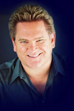 A headshot of Charles Fernandez with brown hair slicked back wearing a dark green collar shirt.