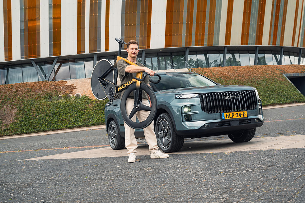 Harrie Lavreysen met fiets over schouder voor een Jaecoo 7. Gebouw op achtergrond met witte en oranje panelen.