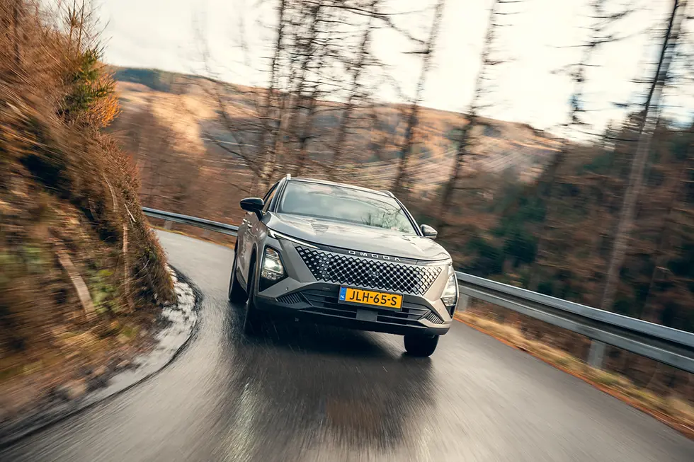Omoda 5 SHS rijdt op natte, bochtige bergweg omgeven door bomen. Zilverkleurige auto. Dynamische en avontuurlijke sfeer.
