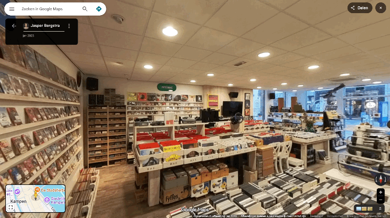 Music store with rows of CDs and LPs in wooden crates. Bright lighting, large display window overlooking the street, quiet atmosphere.