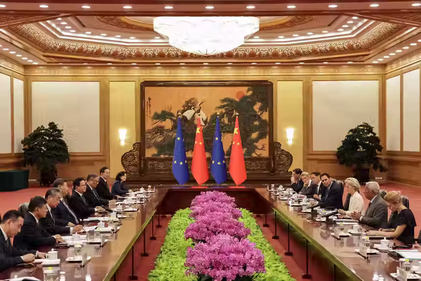 Líderes da China e União Europeia estão em uma sala de conferência com bandeiras de ambas potências com lustre elegante e arranjo floral no centro da mesa 