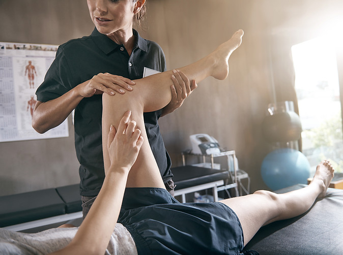 Physiotherapist assessing a patient by testing their hip mobiity while the patient points to the pain on their leg