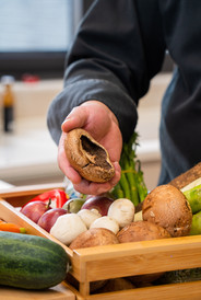 Arm holding mushroom above crate of vegetables