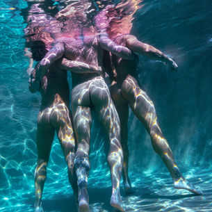 Backside of friends, swimming underwater in pool