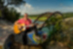 Austin Rosenthal plays a guitar sitting on a graffitied boulder with Austin's PennyBacker Bridge in the background