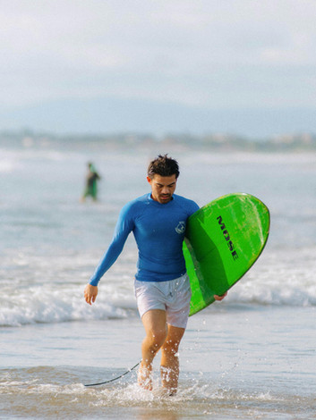 Beginner surfer walking out of the water with surfboard under arm after lesson
