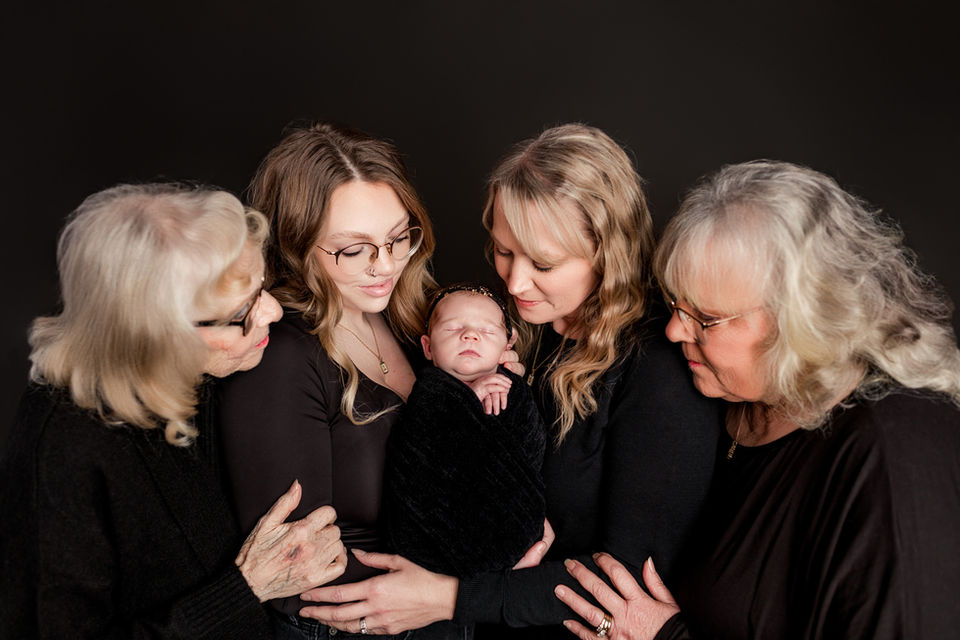 4 women looking at the newborn girl in the center of the image.