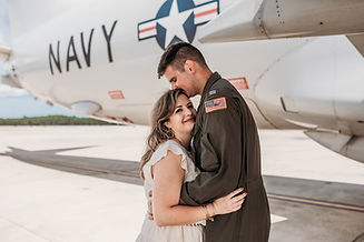 Man in military uniform embracing his wife in front of Naval airplane