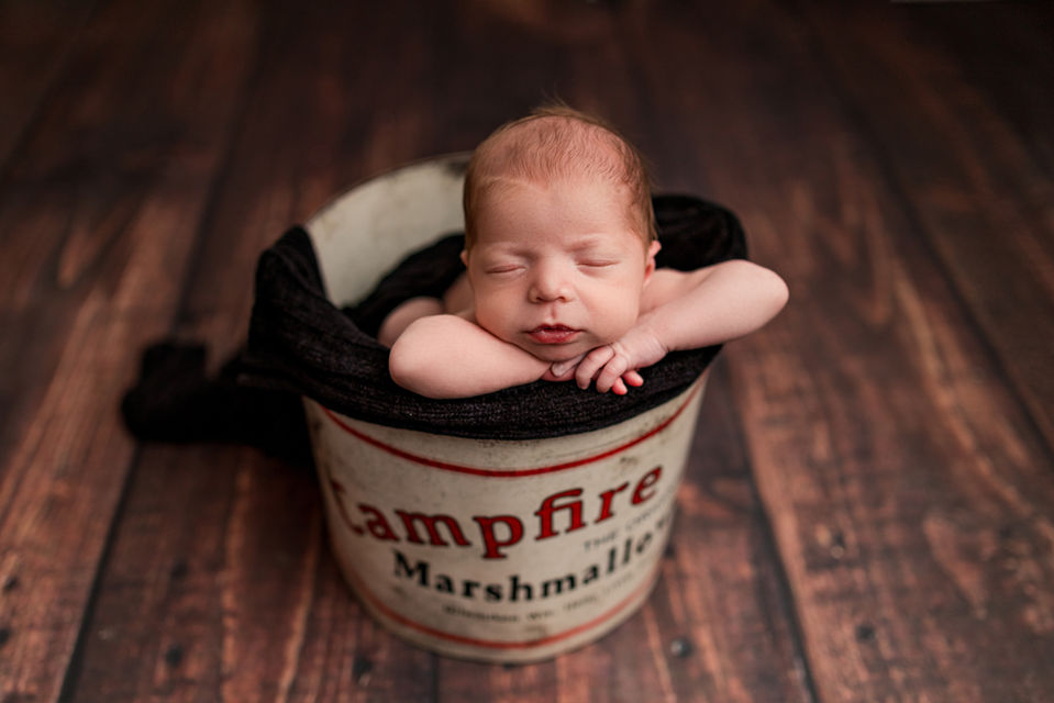 Newborn baby sleeping with chin on hands inside of a bucket