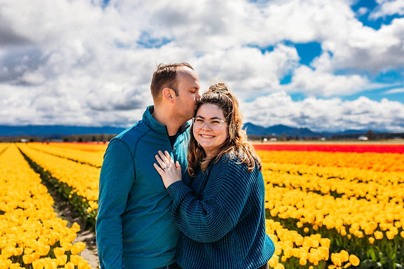 A couple stands together in front of a field of yellow tulips.