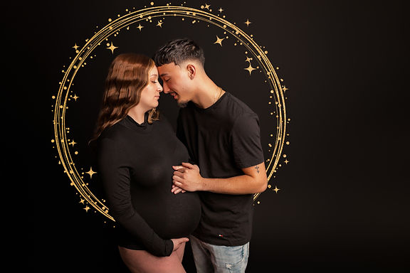 A couple wearing black embraces while woman holds pregnant belly in front of a black background and surrounded by a gold halo.