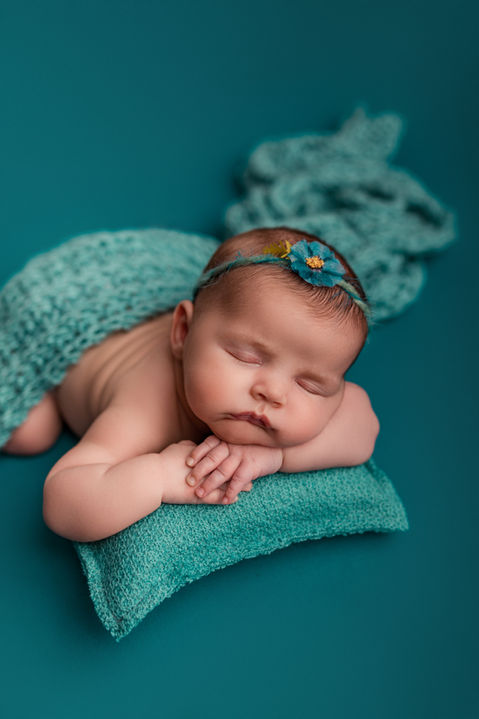 A newborn baby girl sleeping on her stomach with her chin on hands on a pillow.
